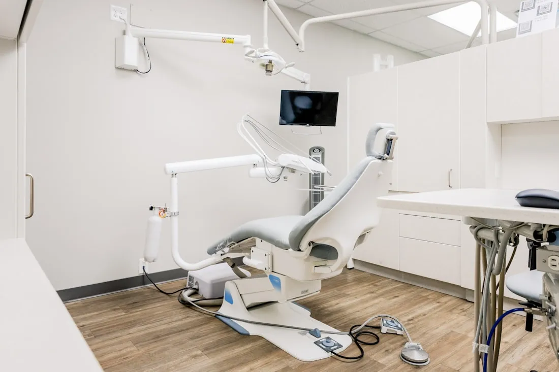 An empty dental operatory with chair, overhead light, monitor and cabinetry.