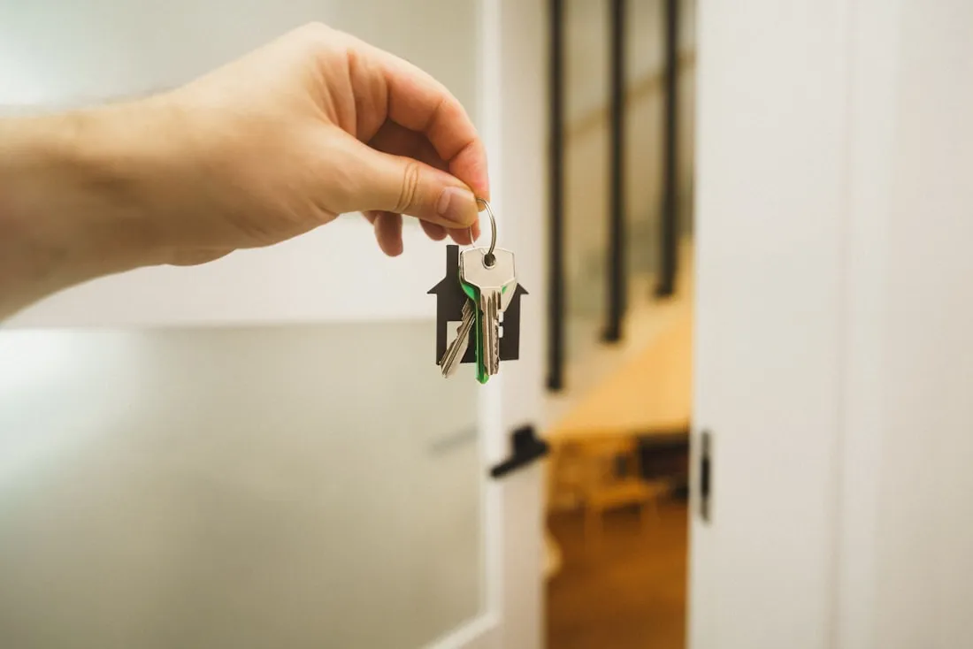 A hand holding a set of house keys in an open doorway.